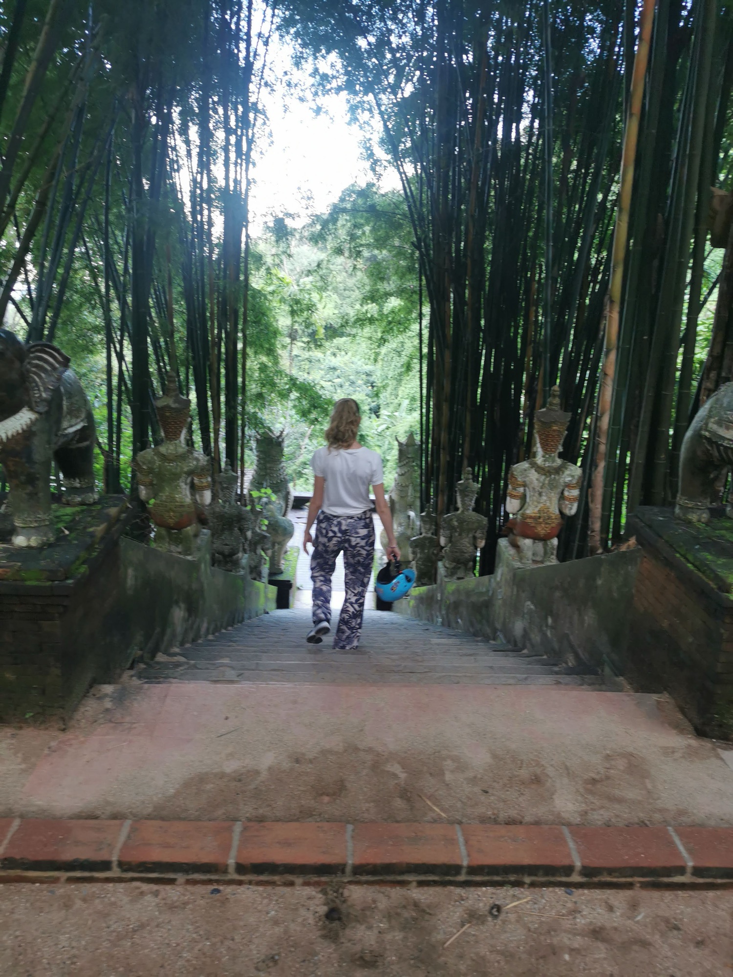 Laura bajando las escaleras entre bambú y estatuas del Wat Pha Lat, en Chiang Mai