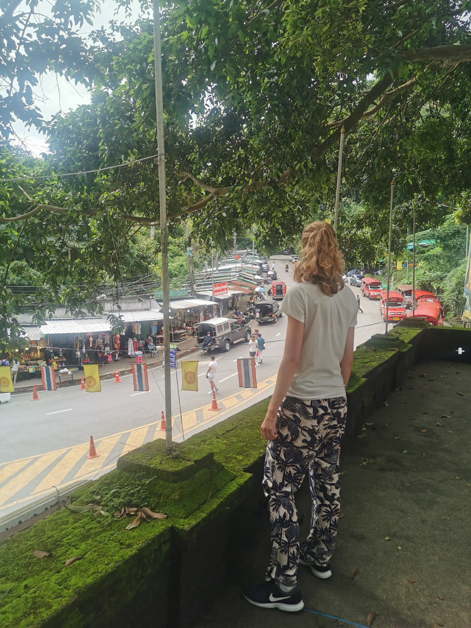 Laura de espaldas junto a la carretera de Doi Suthep, con los songthaews rojos aparcados