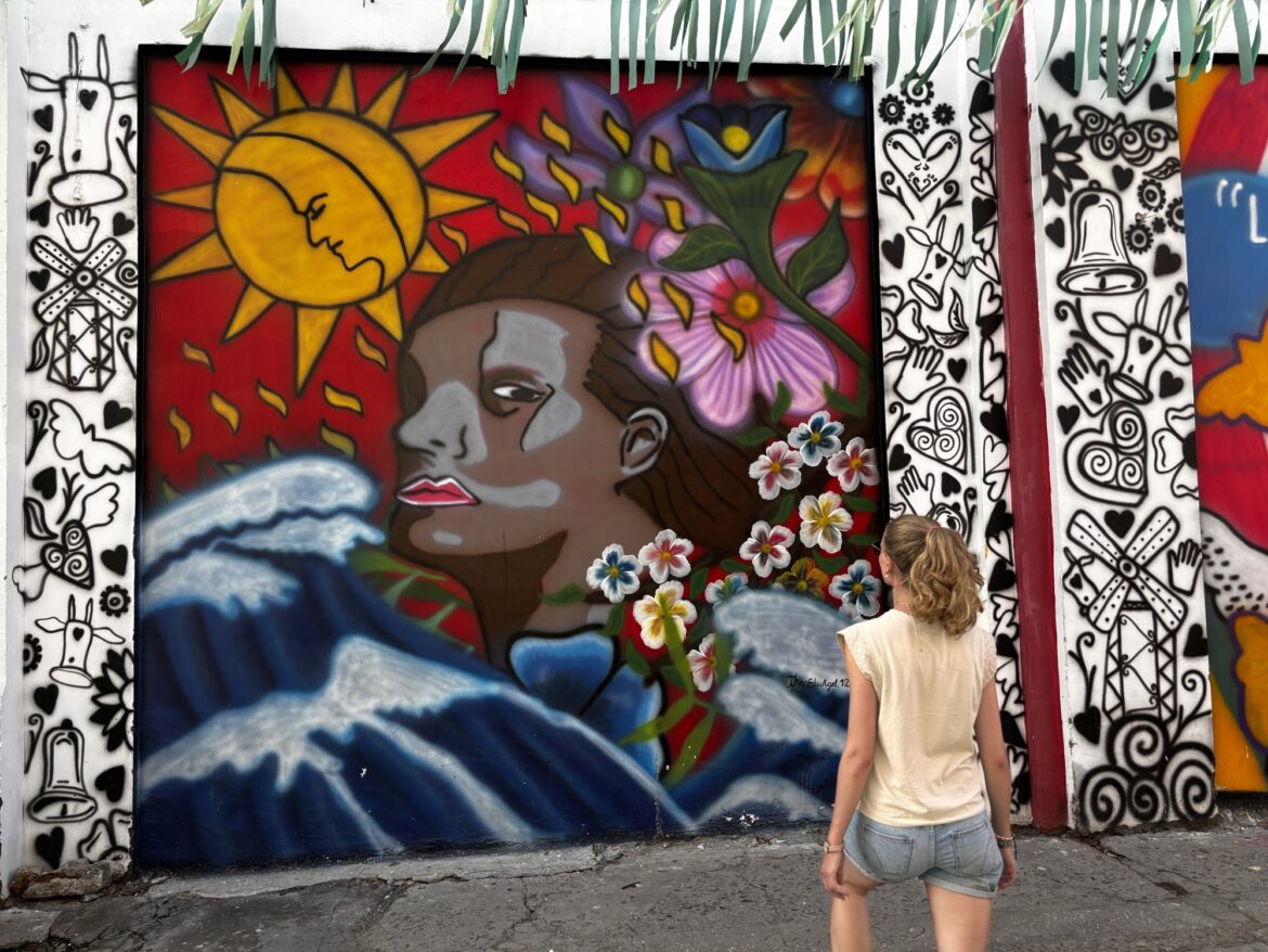 Laura mirando un mural de una mujer con flores y olas en el centro de Santa Marta