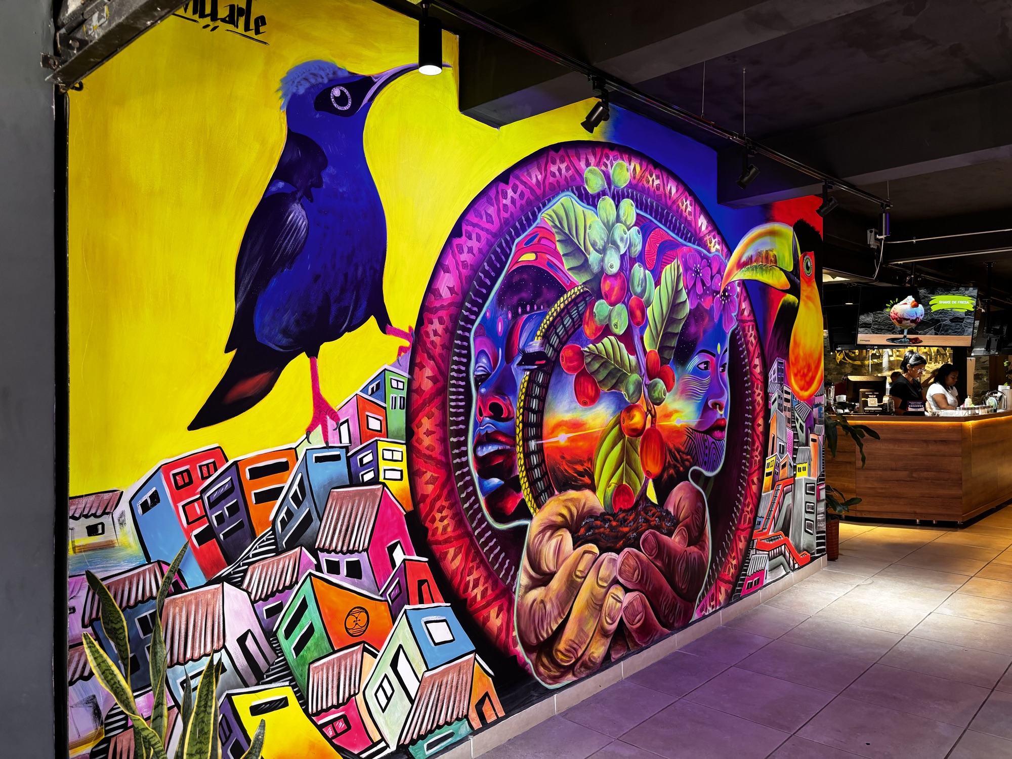Mural de colores con un colibrí y casas de la Comuna 13 en un local de Medellín
