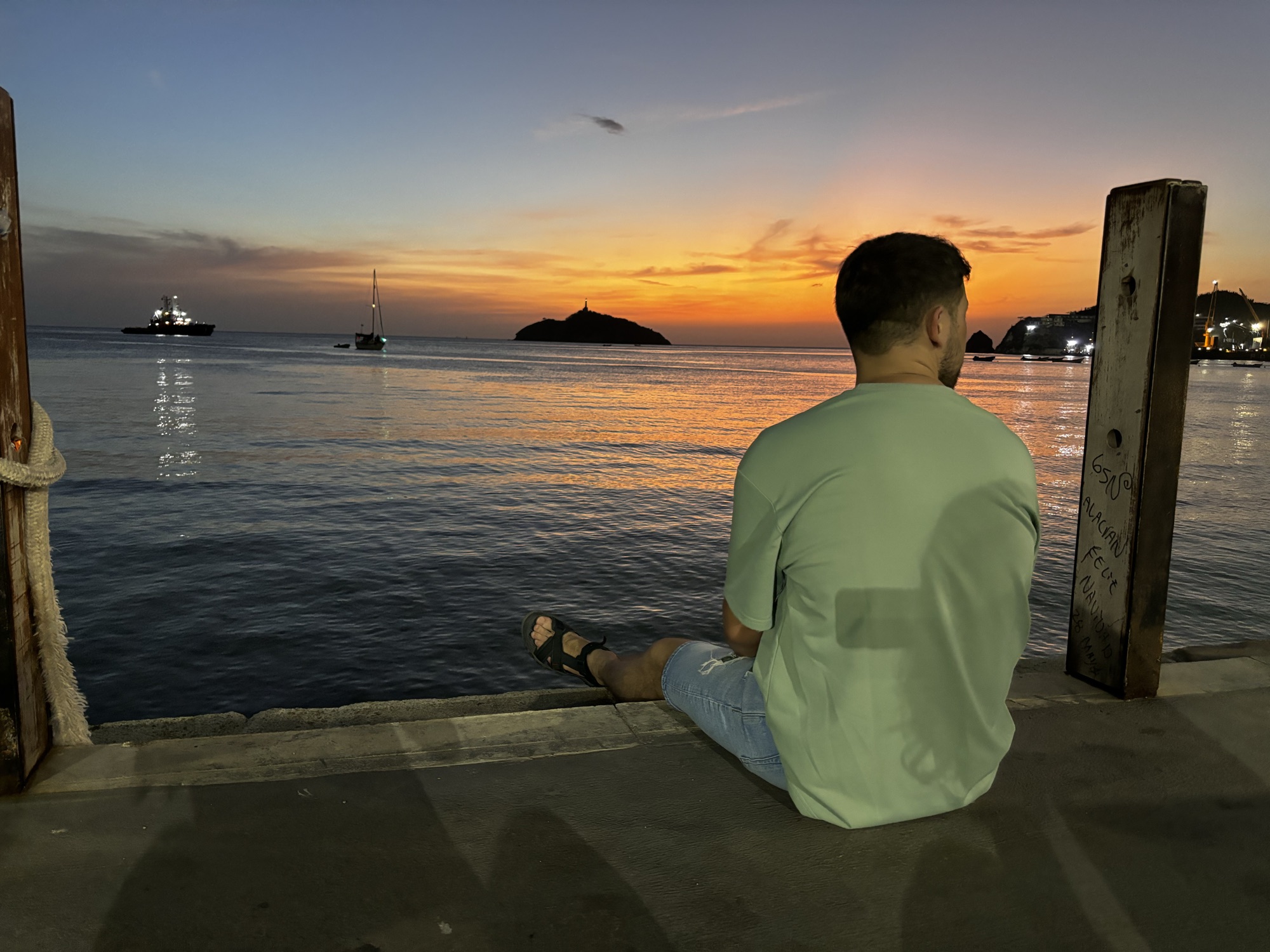 Pablo sentado en el Malecón de Santa Marta viendo la puesta de sol sobre la bahía
