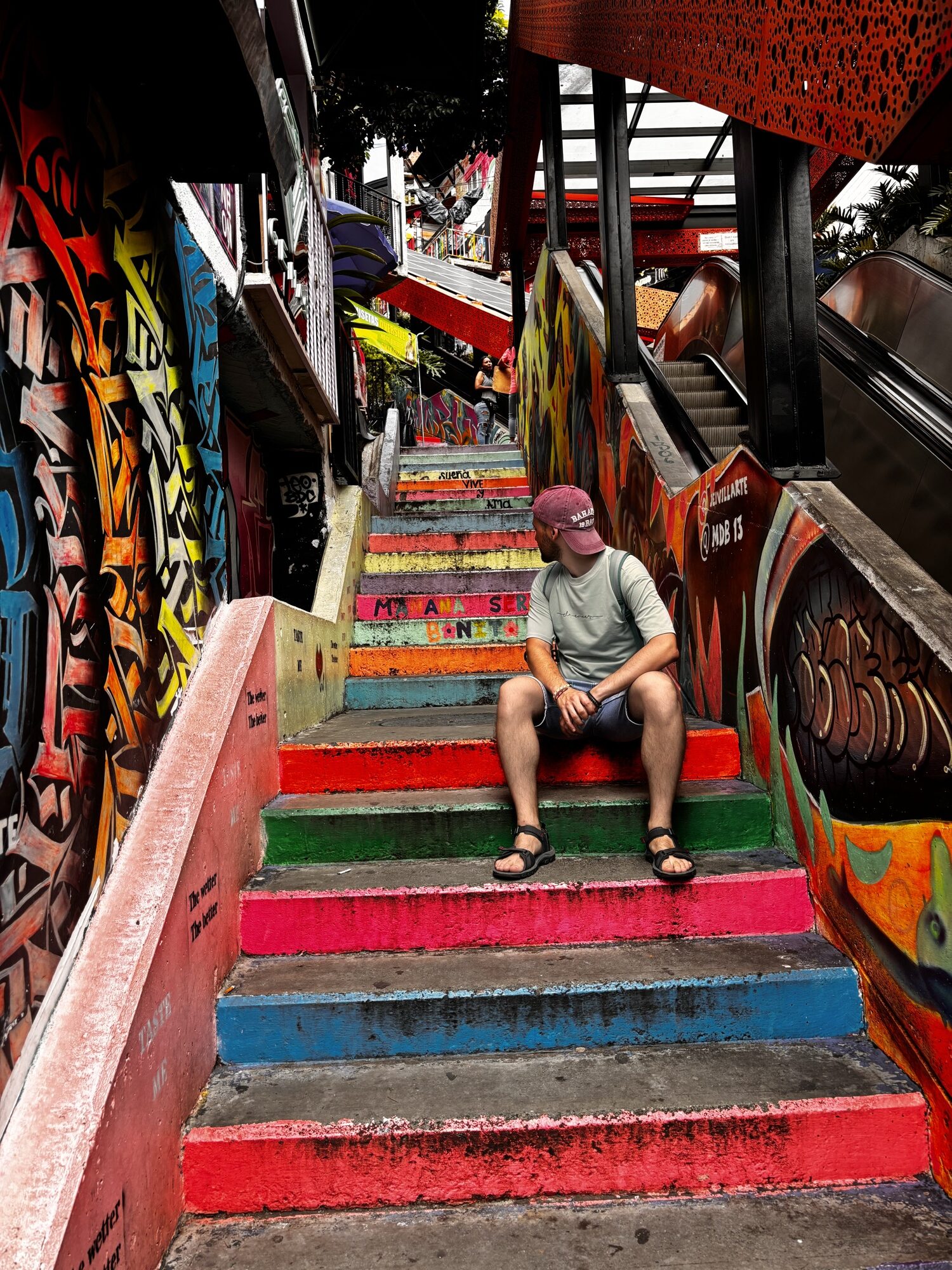 Pablo sentado en las escaleras de colores junto a las escaleras eléctricas de la Comuna 13